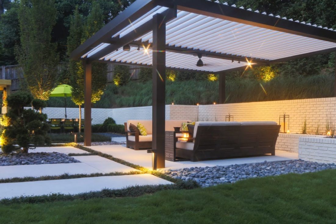 A white louvered patio covering a well manicured backyard patio. 