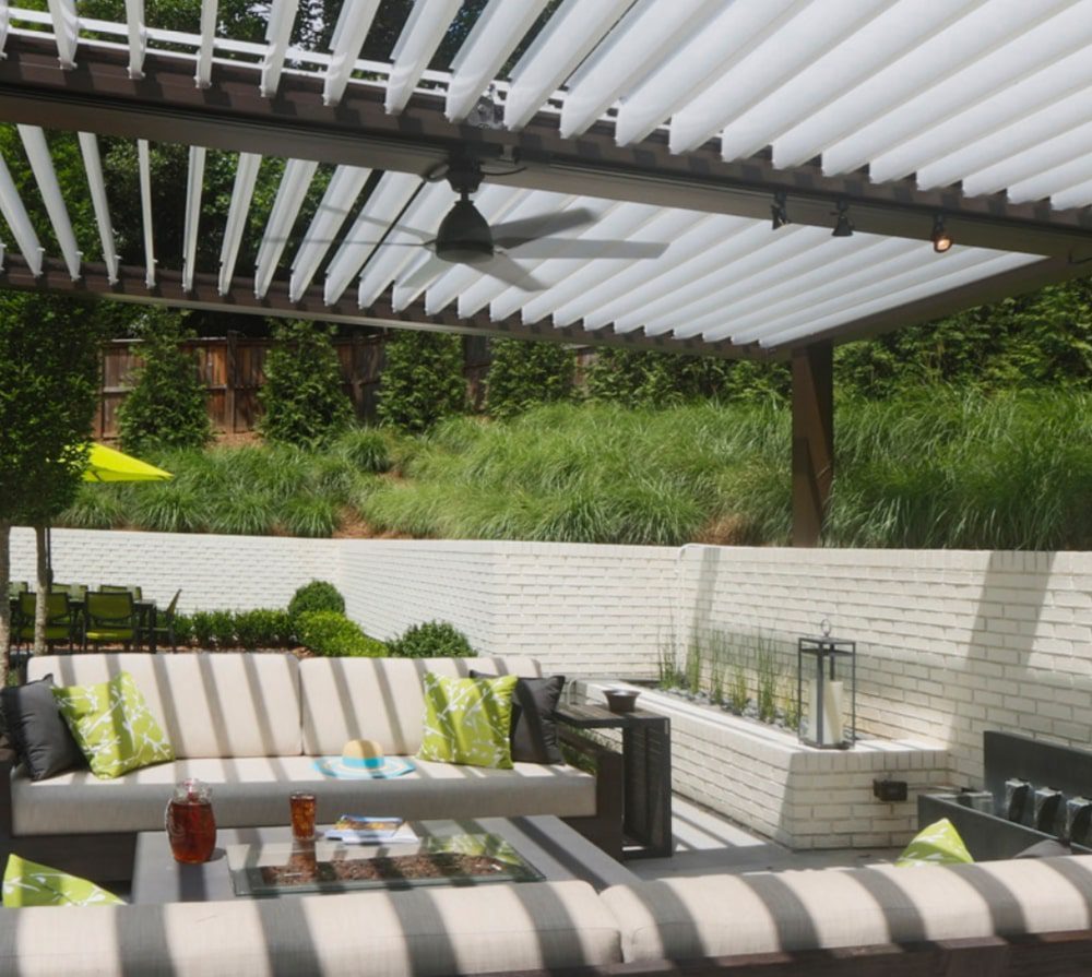 White louvered patio covering a backyard patio with a white brick planter