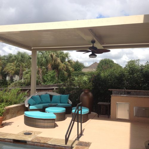 A backyard patio with bbq grill being shaded by an equinox louvered porch cover