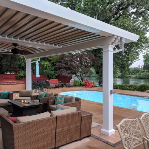 An equinox patio covering provides shading to a residential backyard overlooking a lake