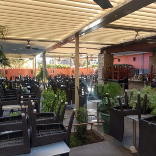 A restaurant outdoor seating area is shaded by an equinox louvered roof system that is closed to block the sunlight