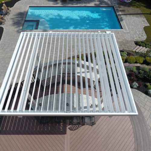 a motorized pergola with open louvers provides shade to a residential pool area