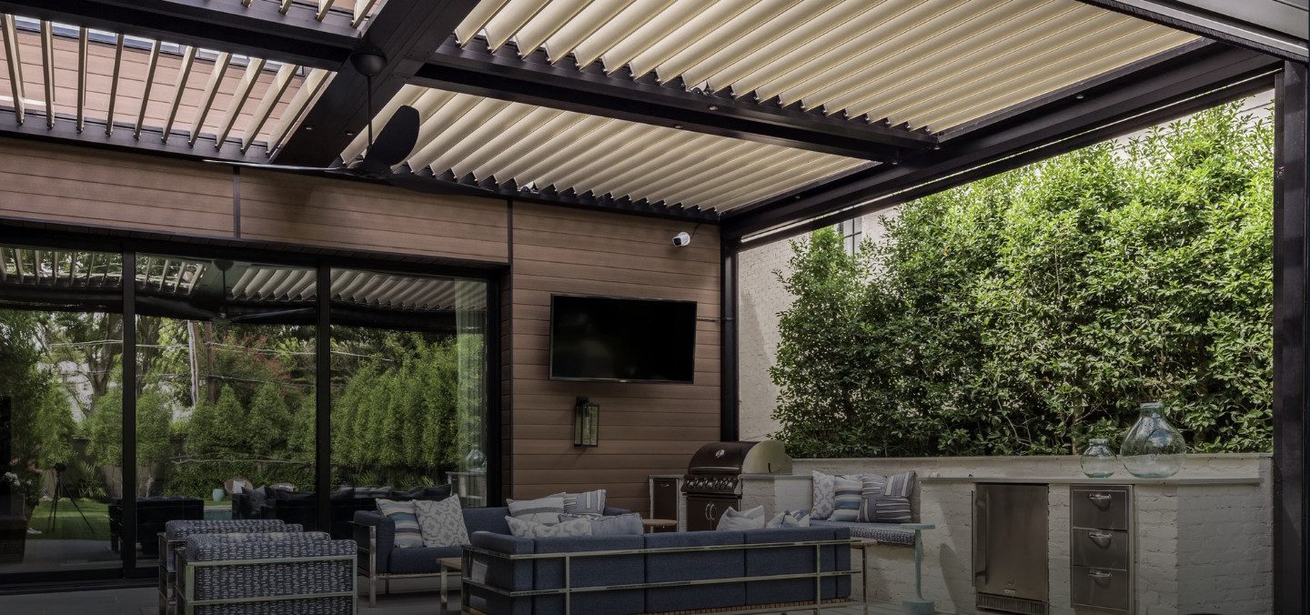 an outdoor seating area is shaded by a motorized pergola with closed louvers