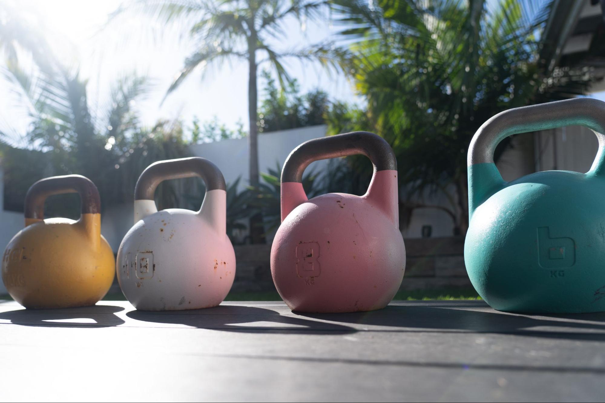Four Kettlebell weights backyard home gym yellow white pink aqua.